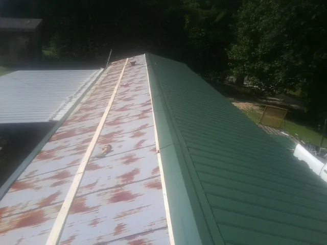 Old rusted panels beside newly installed green metal roofing — Wind Damage Roof Repair by Roofing Brothers in Troutville